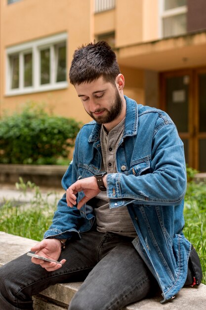 Homem barbudo olhando para relógios enquanto segura o smartphone