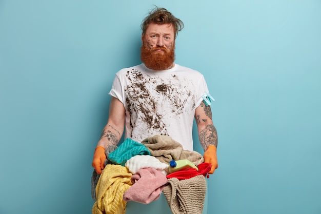 Foto grátis homem barbudo segurando um cesto de roupa suja, sobrecarregado com as tarefas domésticas