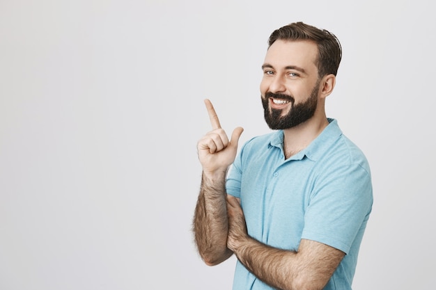 Foto grátis homem barbudo sorridente apontando para o canto esquerdo superior