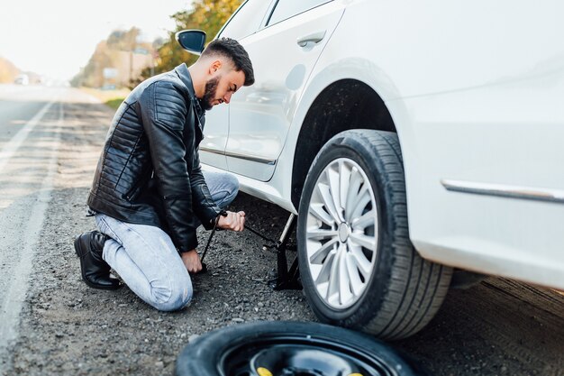 Homem barbudo trocando o pneu do carro