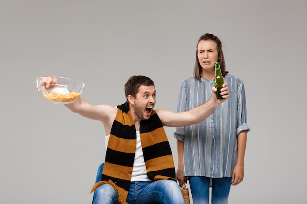 Homem bebendo cerveja, assistindo futebol, chateado mulher em pé atrás, chorando