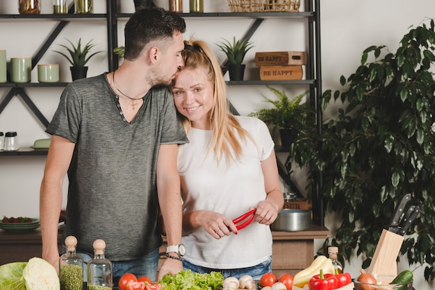 Foto grátis homem, beijando, dela, namorada, testa, segurando, vermelho, pimentões, em, cozinha