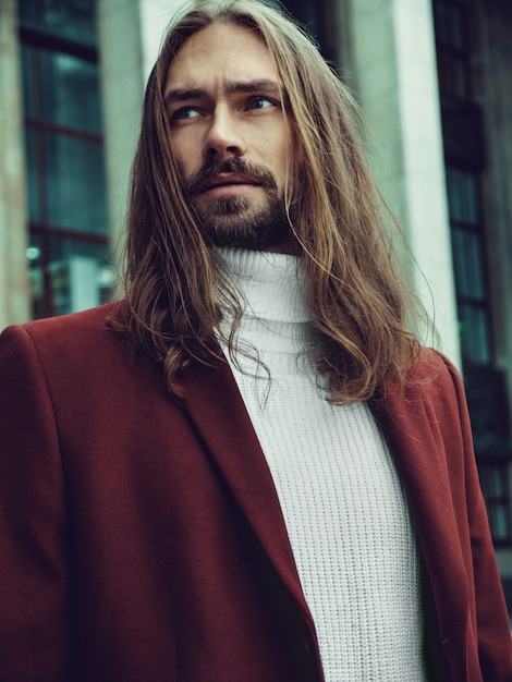 Homem bem vestido confiante bonito com barba posando ao ar livre, olhando para longe. elegante modelo masculino rico em casaco de inverno vermelho e camisola branca