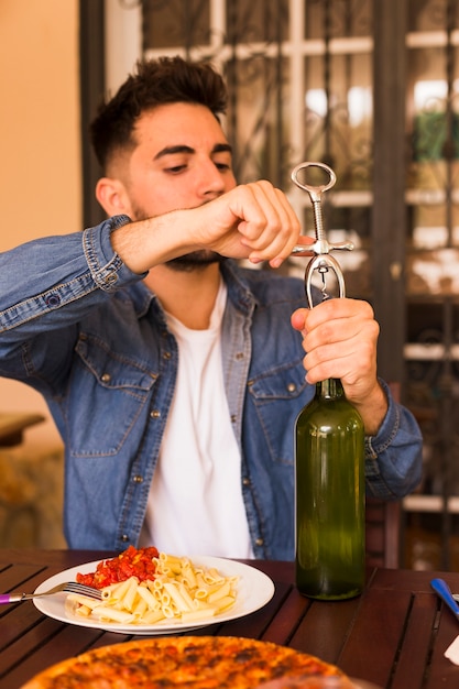 Homem bonito, abrindo a garrafa de álcool com abridor