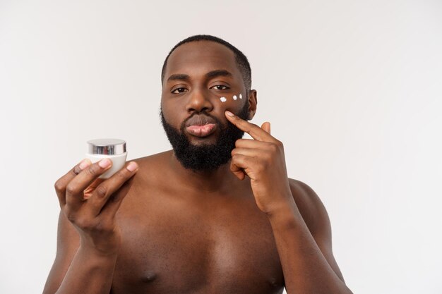 Homem bonito africano aplicando creme no rosto conceito de cuidados com a pele do homem