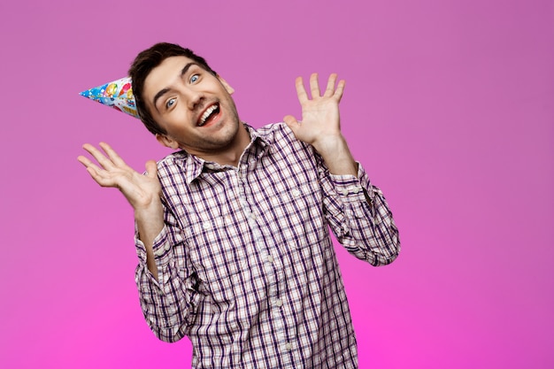 Foto grátis homem bonito alegre sorrindo, regozijando-se ao longo da parede roxa. festa de aniversário.