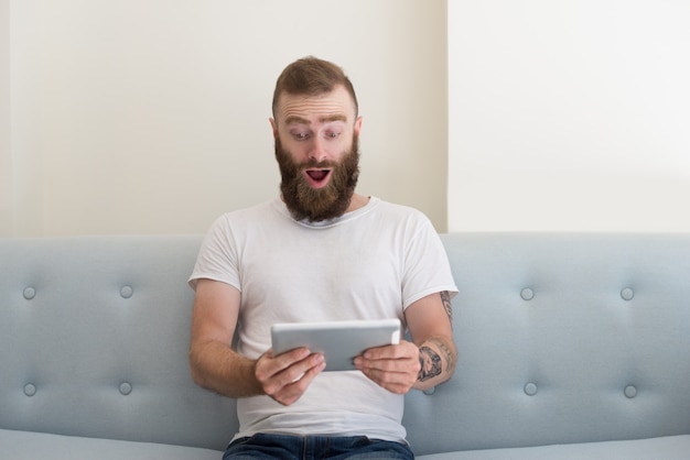 Homem bonito animado com tatuagem assistindo vídeo no tablet