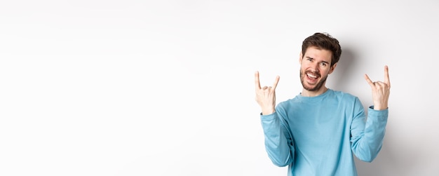 Homem bonito animado comemorando se divertindo e mostrando o gesto de rock nos chifres aproveitando a festa sorrindo