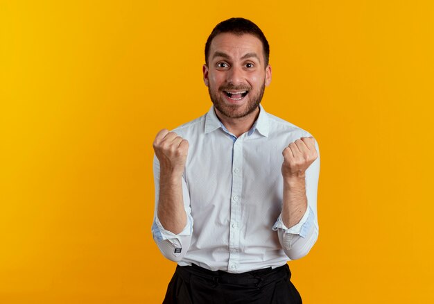 Homem bonito animado mantendo os punhos parecendo isolados na parede laranja