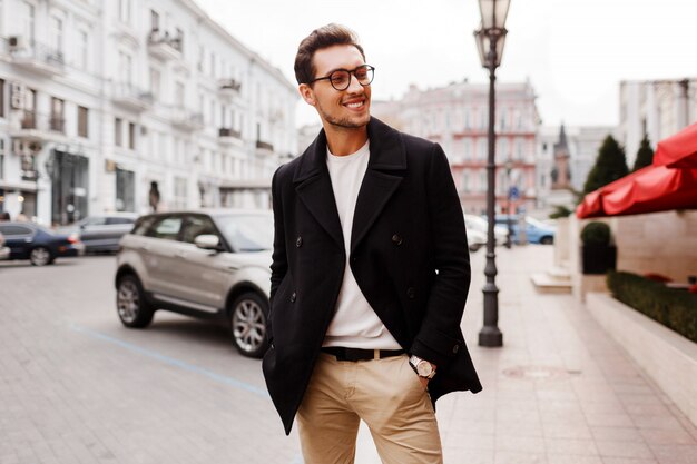 Homem bonito bem sucedido a sorrir numa jaqueta posando na rua. Tendências da moda masculina de outono.