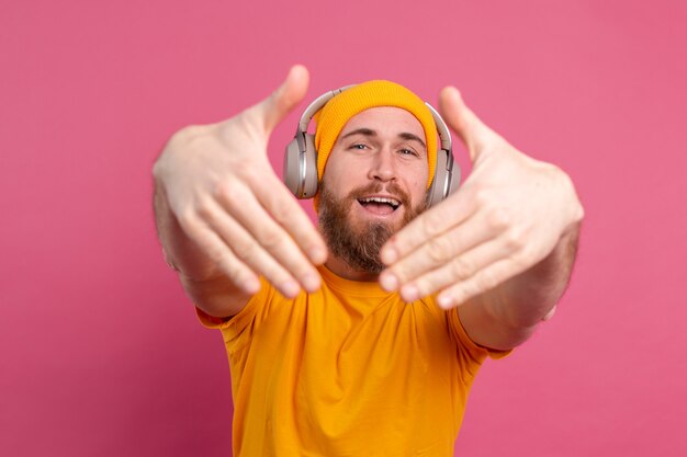 Homem bonito casual ouvindo música com fones de ouvido isolados no fundo rosa