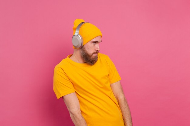 Homem bonito casual ouvindo música com fones de ouvido isolados no fundo rosa