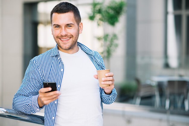 Homem bonito com café e smartphone