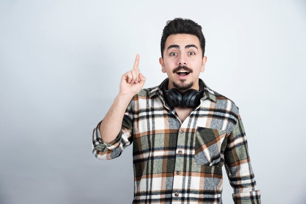 homem bonito com fones de ouvido apontando sobre uma parede branca.