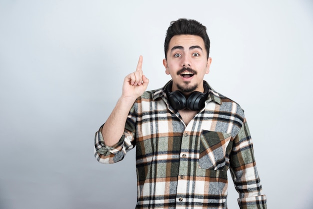 homem bonito com fones de ouvido apontando sobre uma parede branca.