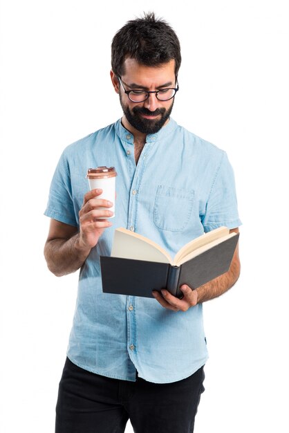 Homem bonito com óculos azuis, livro de leitura e beber café