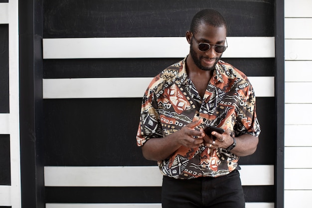 Foto grátis homem bonito com óculos escuros usando smartphone moderno ao ar livre