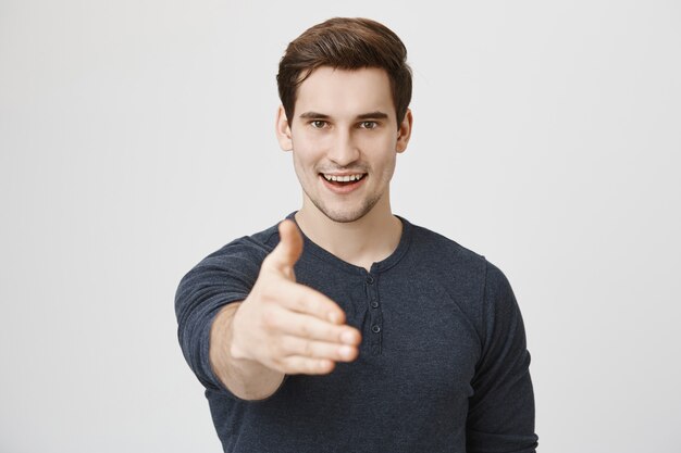 Homem bonito confiante estendendo a mão para um aperto de mão e sorrindo determinado