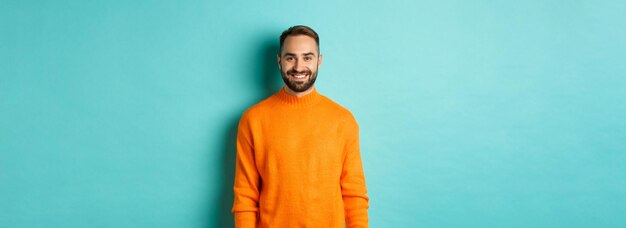 Homem bonito de estilo de vida com suéter laranja sorrindo para a câmera cara feliz expressão alegre standi