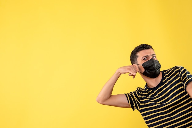 Homem bonito de frente para a máscara preta, fazendo sinal de me chamar de fundo amarelo isolado