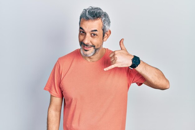 Homem bonito de meia-idade com cabelos grisalhos vestindo camiseta casual sorrindo fazendo gesto de telefone com a mão e os dedos como falar ao telefone. comunicar conceitos.