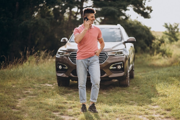 Foto grátis homem bonito, de pé ao lado de seu carro na floresta