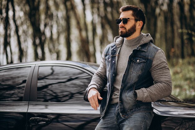 Homem bonito, de pé ao lado do carro no parque