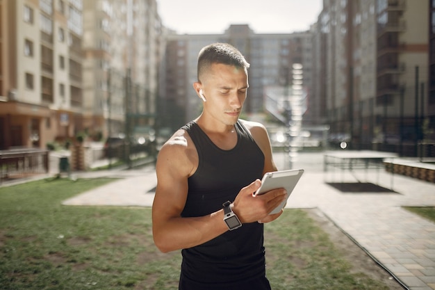 Homem bonito, de pé em um parque com fones de ouvido e um tablet