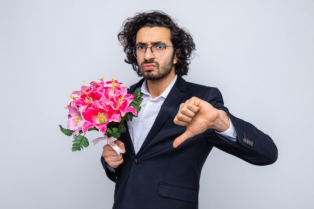 Homem bonito de terno com buquê de flores parecendo descontente mostrando os polegares para baixo