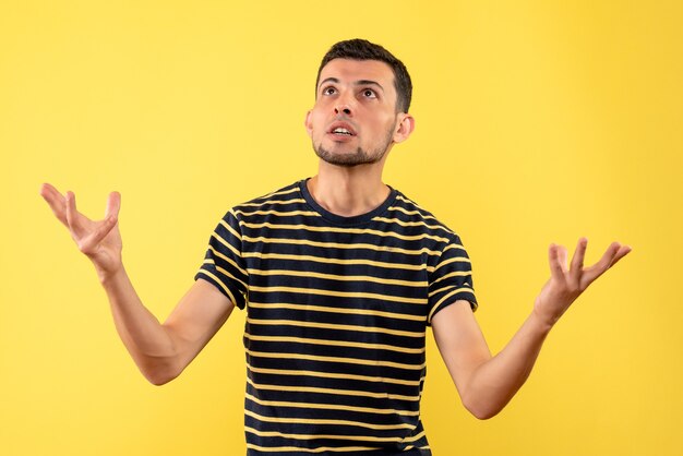 Homem bonito de vista frontal em uma camiseta listrada em preto e branco olhando para o teto em um fundo amarelo isolado