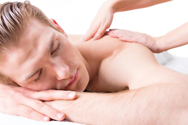 Homem bonito, deitado em um salão de spa, desfrutando de uma massagem profunda nas costas.