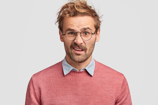 Homem bonito descontente franze a testa com descontentamento, sente aversão ao notar algo nojento, tem penteado na moda