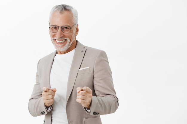 Homem bonito e bem sucedido sênior de terno apontando os dedos e sorrindo atrevido