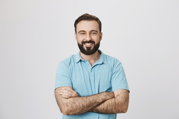 Homem bonito e confiante sorrindo com as mãos cruzadas no peito