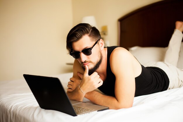 Homem bonito e elegante posando ao ar livre em um hotel, deitado na cama