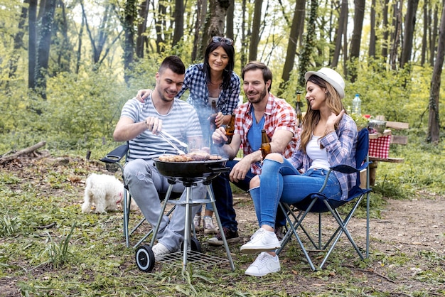 Homem bonito e feliz preparando churrasco ao ar livre para amigos