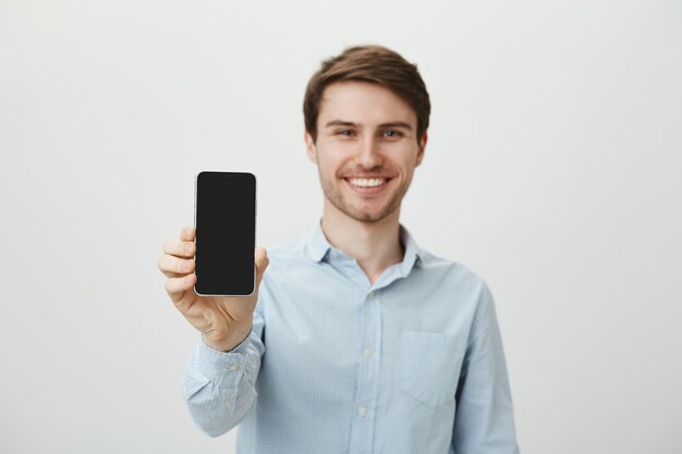 Homem bonito e sorridente mostrando a tela do smartphone