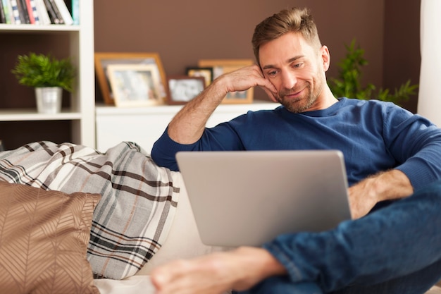 Homem bonito e sorridente relaxando com o laptop em casa