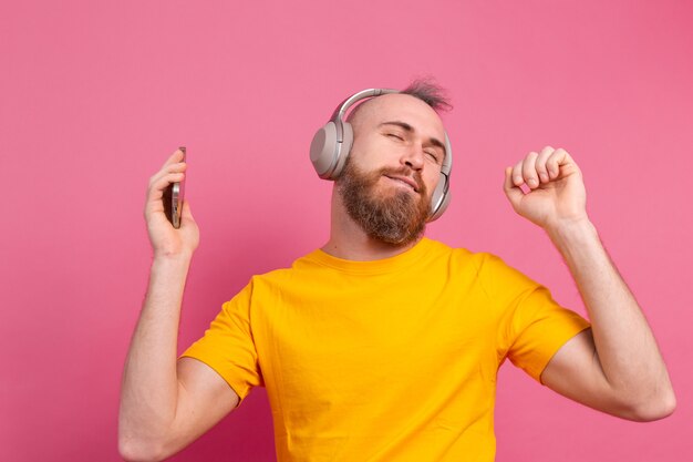 Homem bonito em dança casual com celular e fones de ouvido isolados no fundo rosa