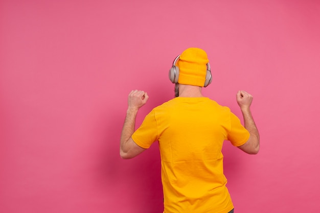 Homem bonito em dança casual com fones de ouvido isolados em fundo rosa