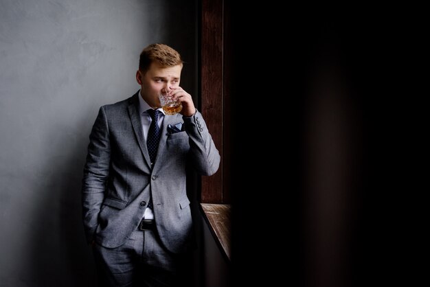 Homem bonito em traje formal é beber álcool e olhando pela janela