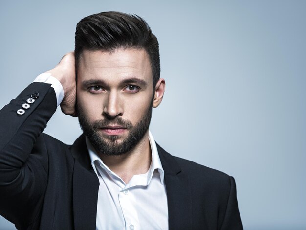 Homem bonito em um terno preto com camisa branca - posando cara atraente com penteado da moda. Homem confiante com barba curta. Menino adulto com cabelo castanho.