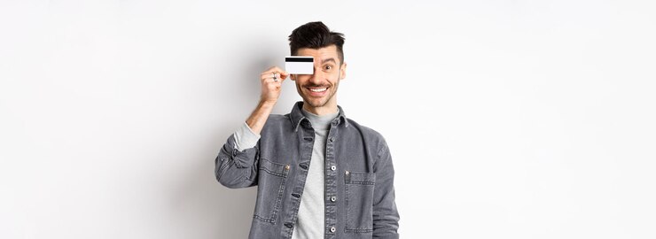 Foto grátis homem bonito feliz com bigode mostra cartão de crédito de plástico no olho sorrindo animado com a câmera em pé