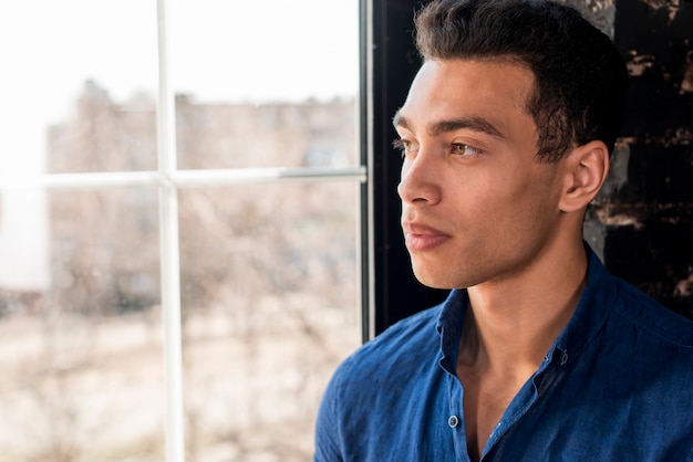 Foto grátis homem bonito jovem pensativo olhando pela janela