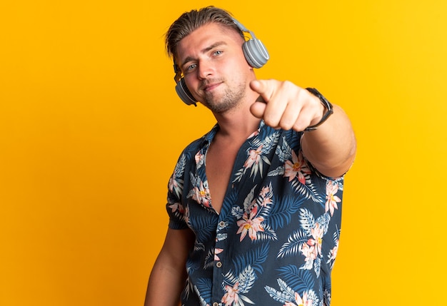 Homem bonito loiro confiante com fones de ouvido apontando para a frente