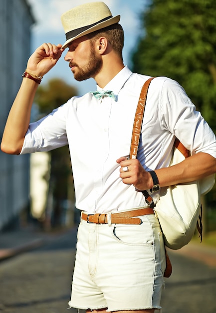 Homem bonito modelo hipster em roupas de verão elegante posando de chapéu com bolsa