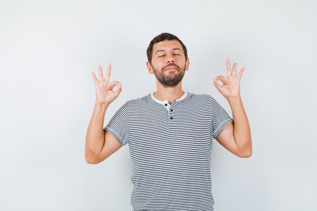 Homem bonito, mostrando o gesto de ioga em t-shirt e parecendo em paz. vista frontal.