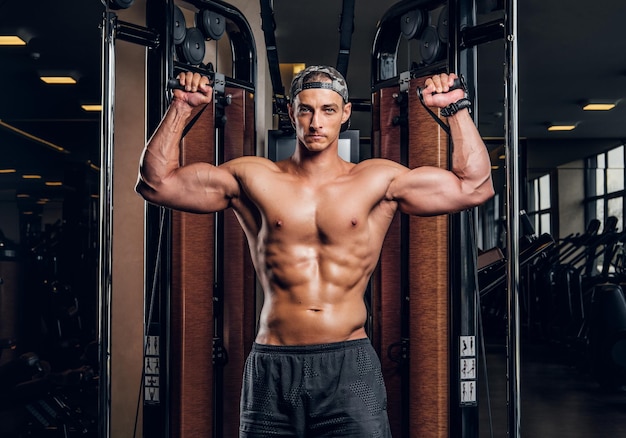 Homem bonito musculoso está fazendo exercícios com aparelhos de treinamento no clube de ginástica escuro.