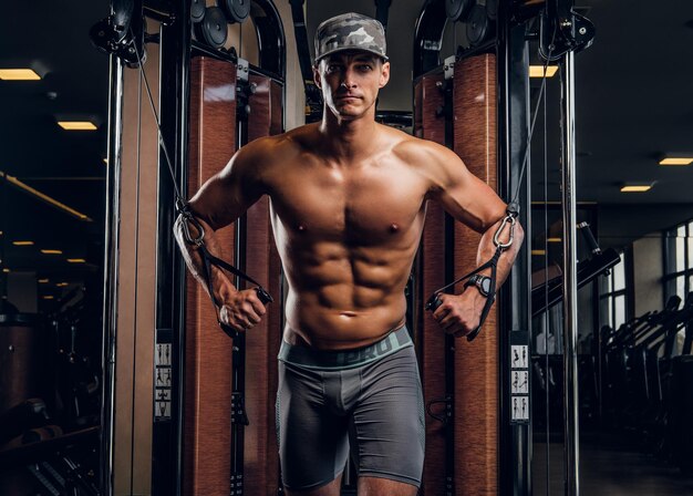 Homem bonito musculoso está fazendo exercícios com aparelhos de treinamento no clube de ginástica escuro.