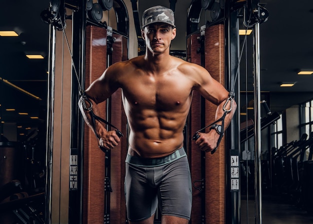 Homem bonito musculoso está fazendo exercícios com aparelhos de treinamento no clube de ginástica escuro.